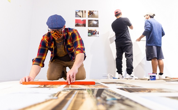 Andrew Cline working on installation with people in the background hanging art.