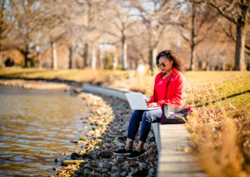 Karena Beckham in MSU Denver swag, working on a laptop in City Park.