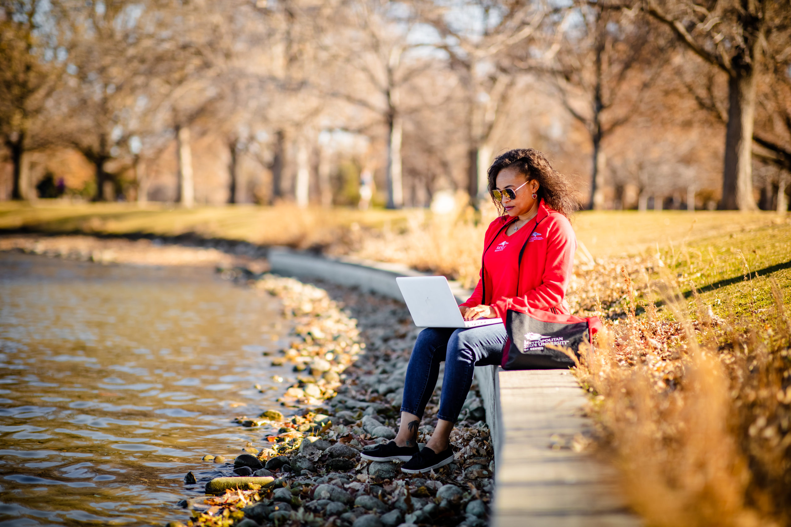 Karena Beckham in MSU Denver swag, working on a laptop in City Park.