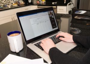 Close up of hands typing on a laptop computer in home kitchen.