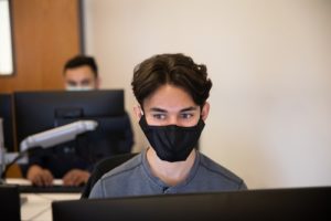 Students wearing masks while working at desktop computers.