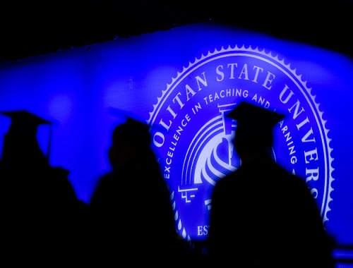 Silhouettes of three students walking toward Commencement stage.