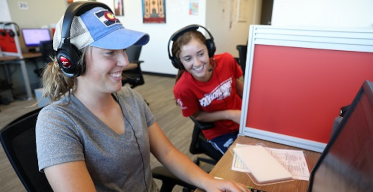 Two call center employees with headsets on working at their desks.