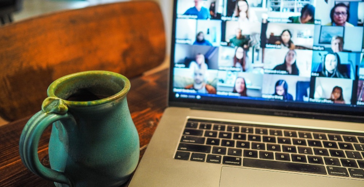 Close up of a mug next to a laptop with a virtual meeting on the screen.