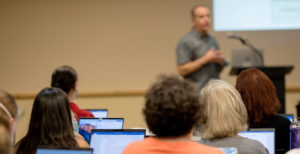 People listening to a speaker at a Faculty Senate meeting.