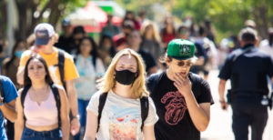 Students walking on Auraria campus with one student in the center of the frame wearing a mask.