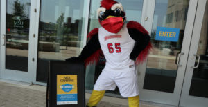 MSU Denver mascot Rowdy wearing a mask and posting next to a mask requirement sign.