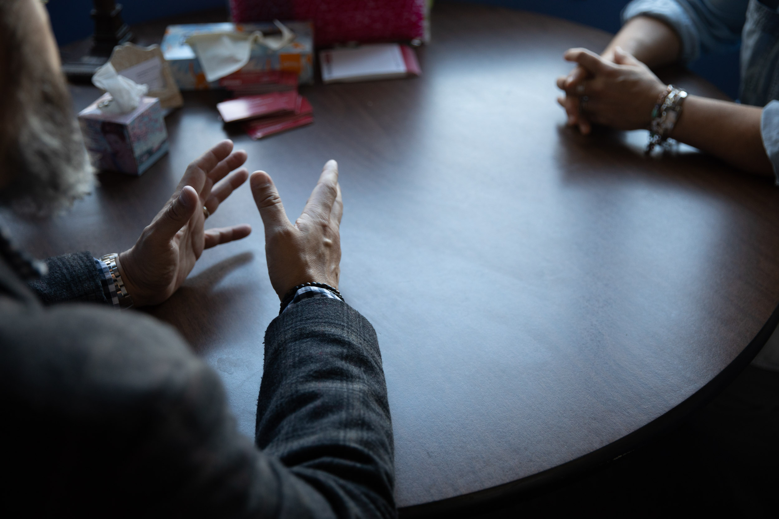 Two people sitting at a table having a conversation; focus is on hands.