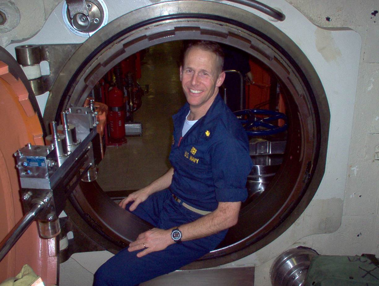 Loring Crepeau, Outstanding Alumni winner sitting in his navy uniform in a submarine on a threshold between two rooms.