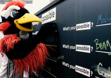 Rowdy Roadrunner mascot at a chalkboard filling out a prompt that says 'What's Your Possible'?