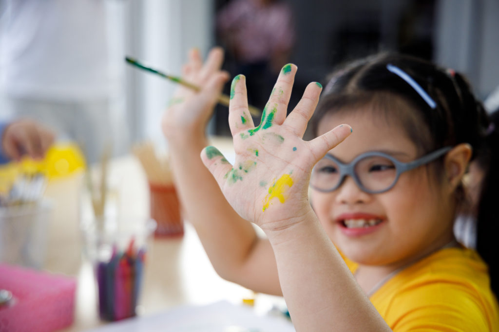 Happy Asian girl with Down's syndrome painting her hand with water color in art class.