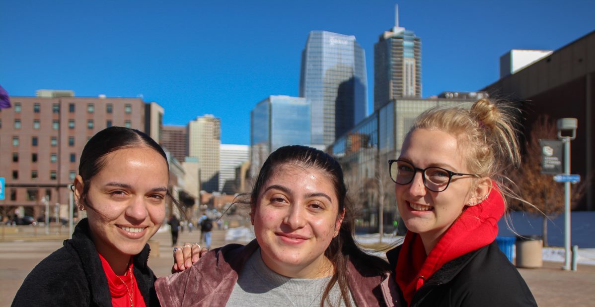 Three students in front of Denver skyline