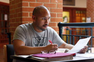 Man sits at table in campus building editing with a red pen.