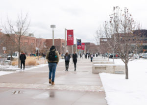 Students walk across campus with snow on the ground and a wet sidewalk