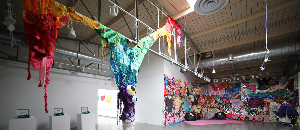 Colorful crocheted fabric installation in an art gallery with high ceilings and industrial features.