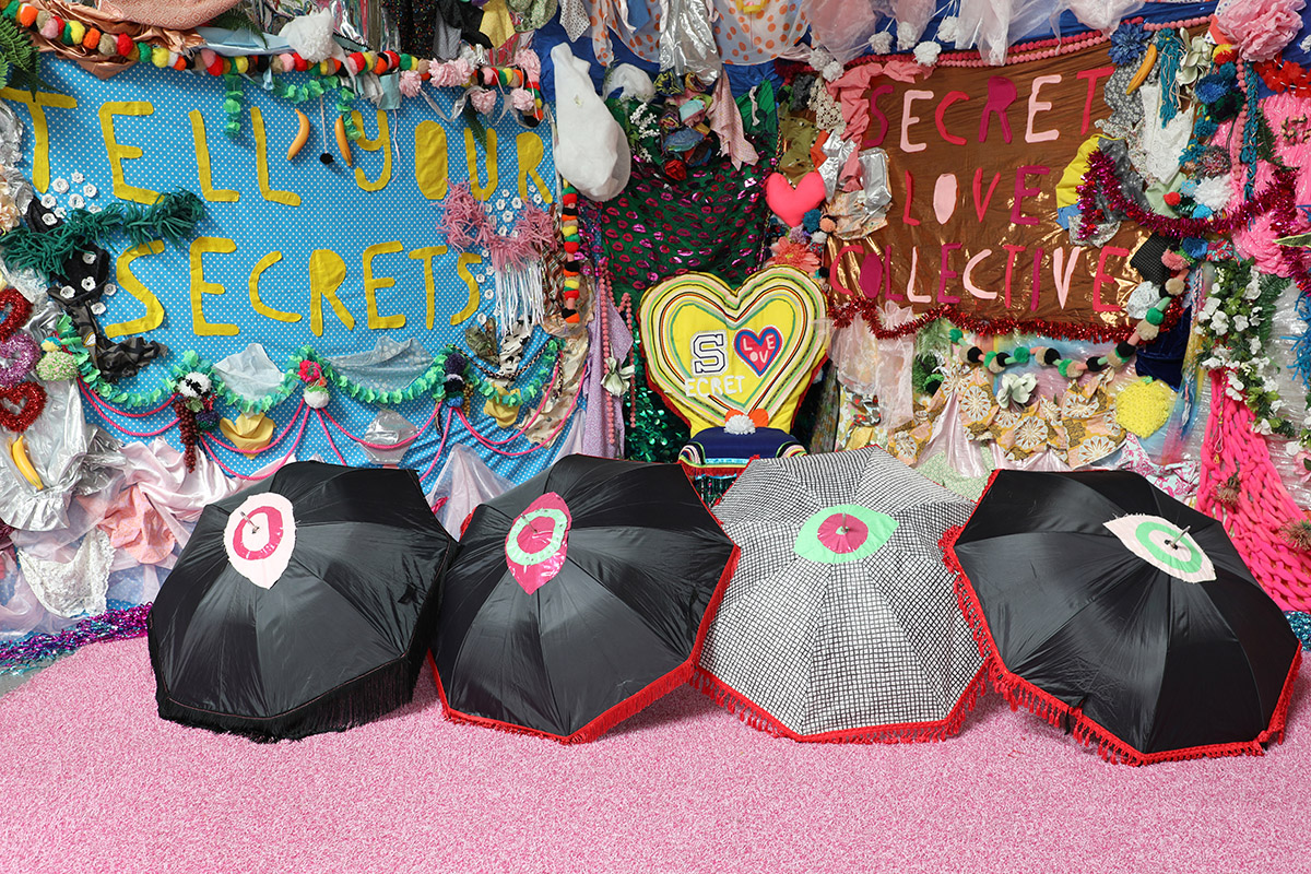 A colorful installation with umbrellas and fabric banners displaying the phrases 