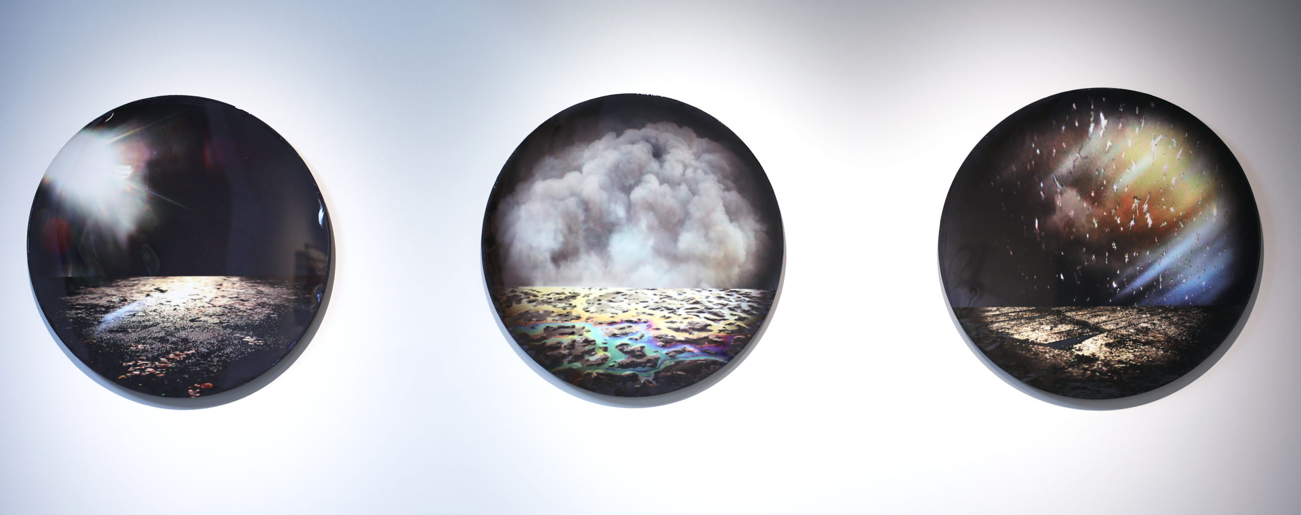 Three circular abstract artworks on a white wall, each depicting different atmospheric scenes.
