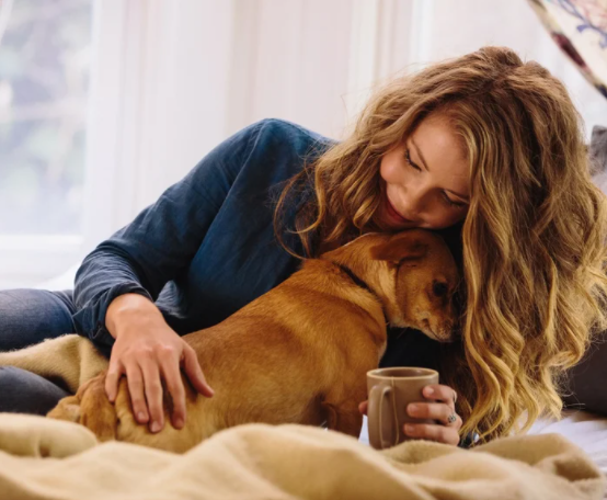 Photo of a woman hugging and petting a dog while holding a mug with their other hand