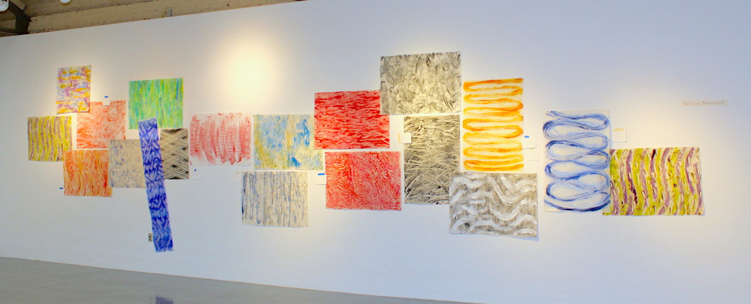 An arrangement of colorful abstract artwork on a white wall.