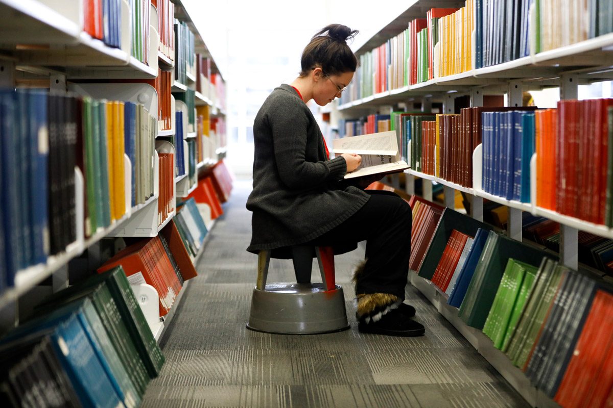 student reading a book in the library between two bookshelves