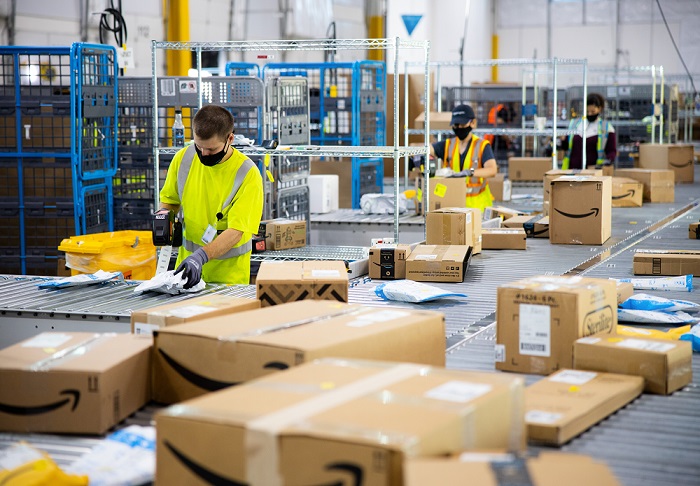 Two socially distanced Amazon workers in a warehouse and wearing masks and gloves.
