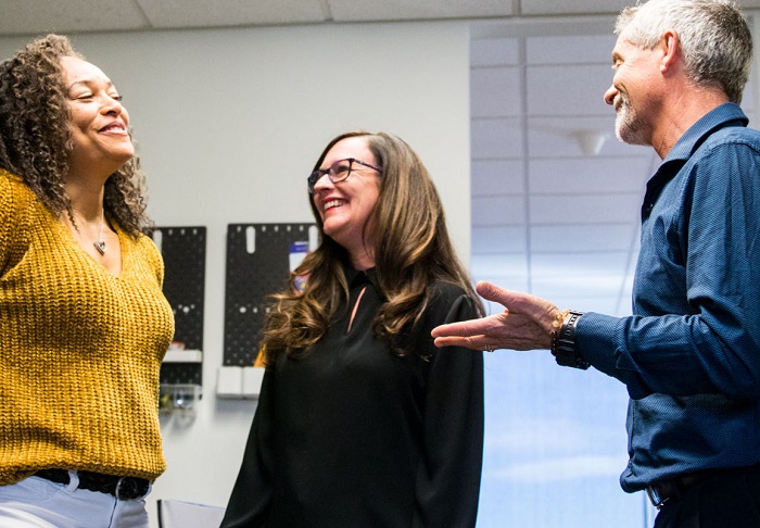 Three Human Resources employees standing together talking and smiling.