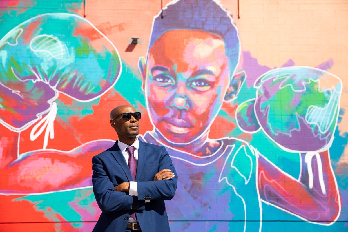 MSU Denver alumnus Eric Williams standing in front of street art of a boy with boxing gloves on his hands.