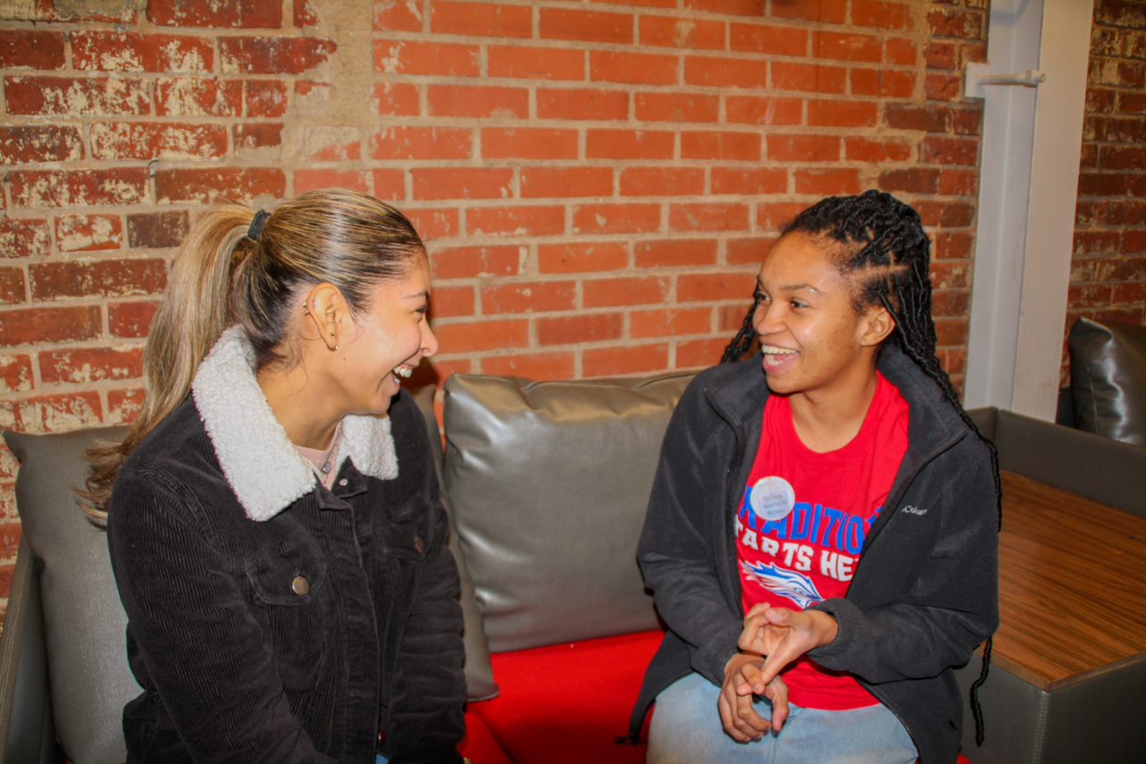 Two students in front of brick wall laughing