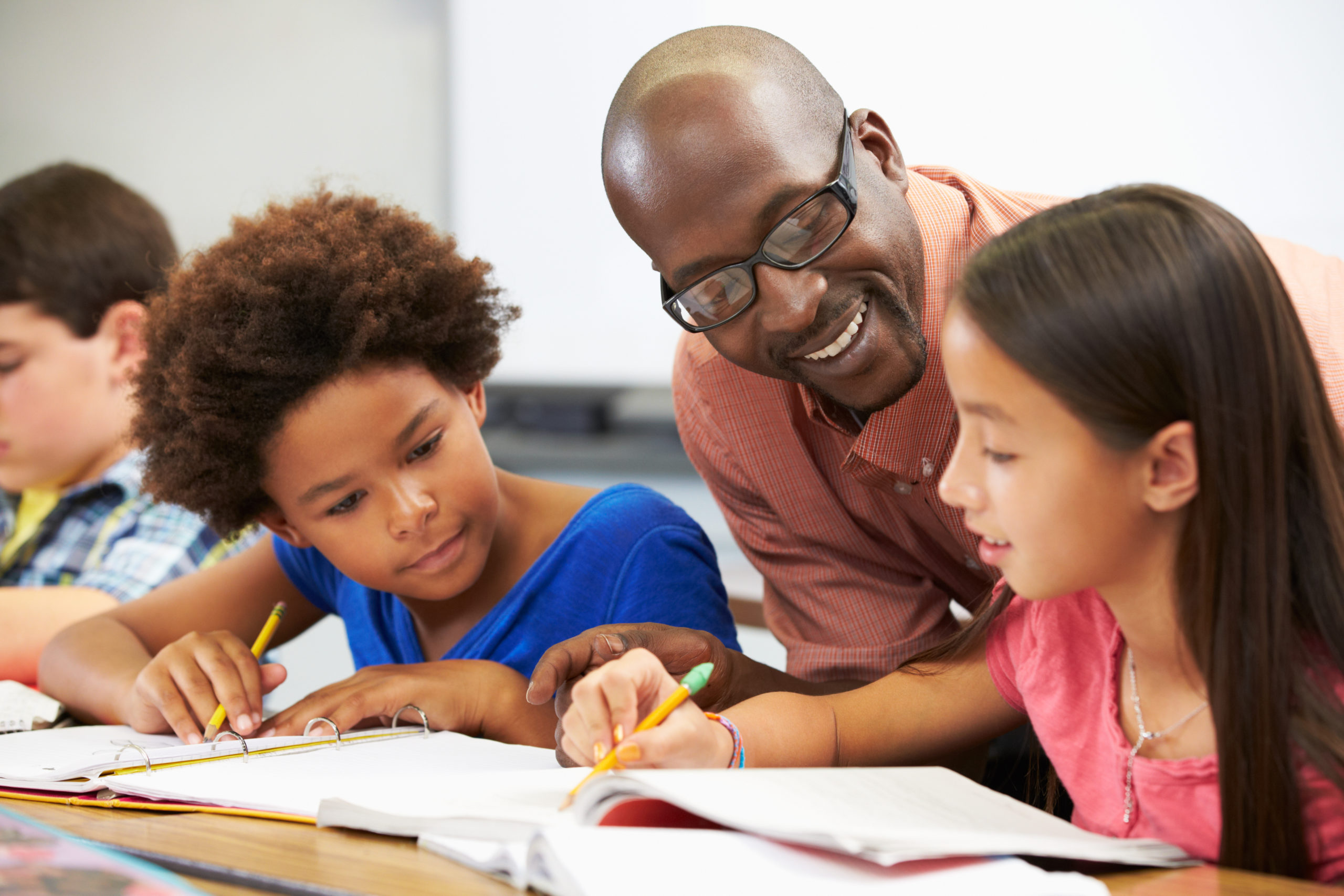 Teacher helping students studying at desks In classroom checking work and smiling.