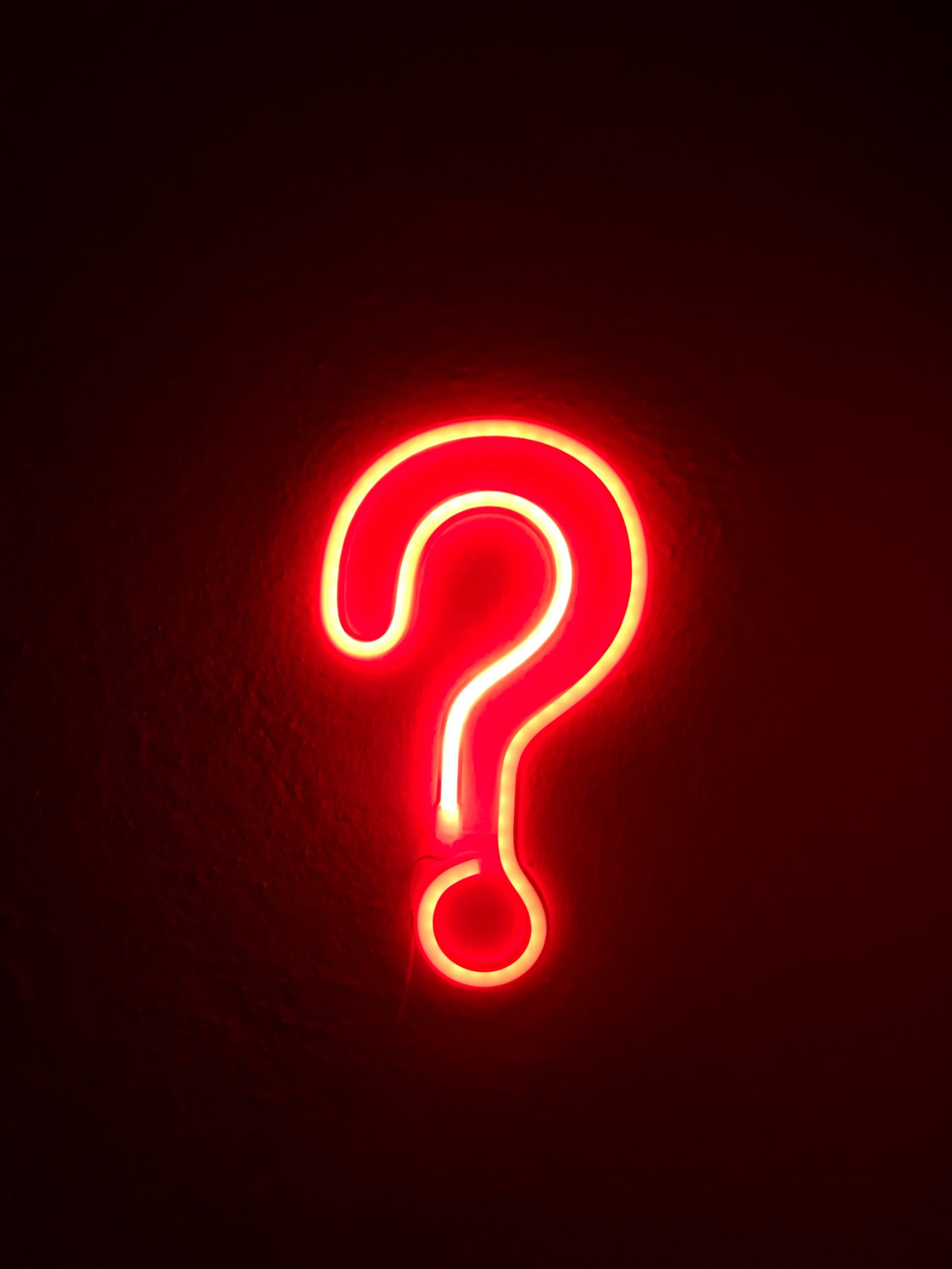 A red neon sign shaped as a question mark against a dark wall