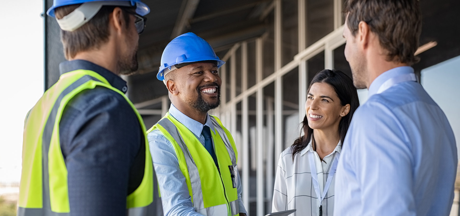 Smiling engineer shaking hands at construction site with happy architect. Handshake between cheerful african construction manager with businessman at bulding site. Team of workers with architects and contractor conclude an agreement with safety uniform.