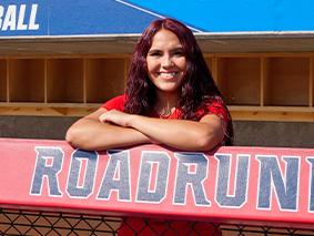Arianna Valdez leaning on a fence with a Roadrunners sign.