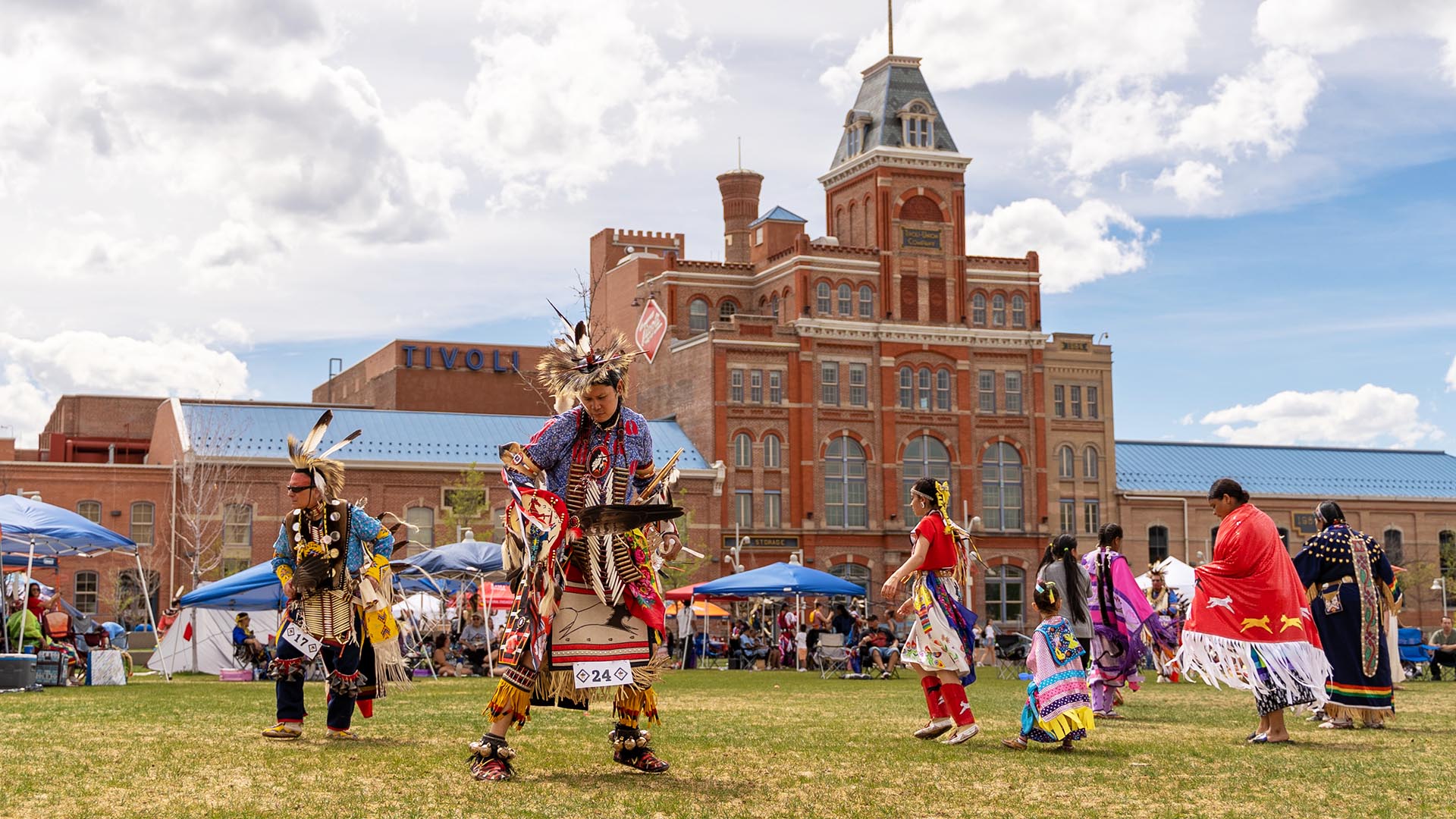 The first annual Auraria Campus Pow wow took place on the Tivoli quad; indigenous students and nation representatives are in dance on the lawn with the Tivoli student union in the background.