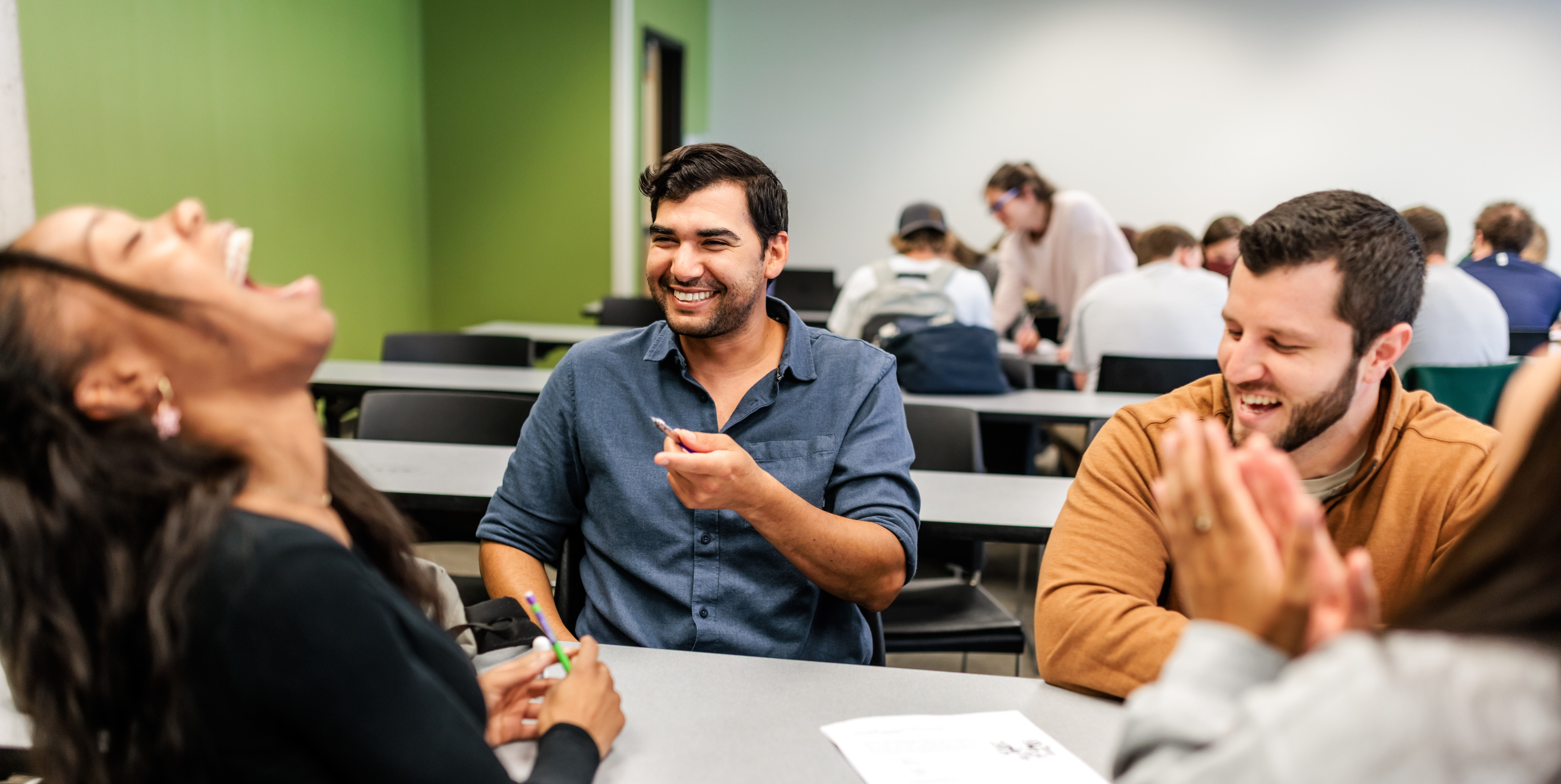 Three students laugh while working in a classroom