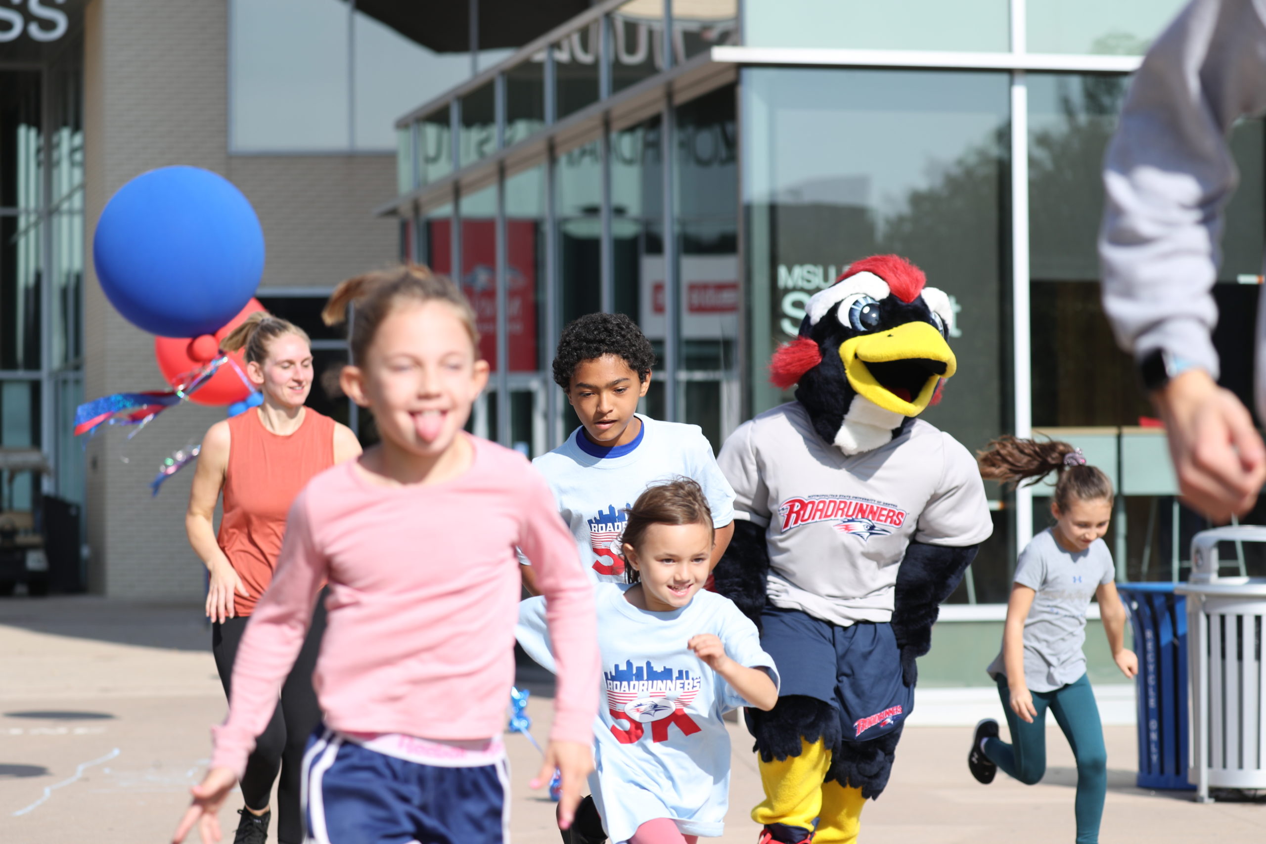 Kids running with Rowdy in front of the Student Success building at the 2021 Roadrunners 5K