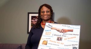 Darlene Sampson standing with a sign covered in social justice advocacy sayings, such as I stand for Black children, GLBT Rights, DACA, Black Lives Matter, Equity for all