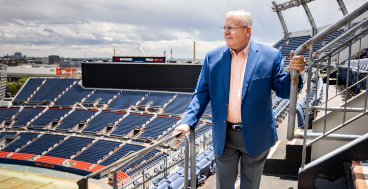 Jim Saccomano looking out over the Empower Field at Mile High stadium from the stands.