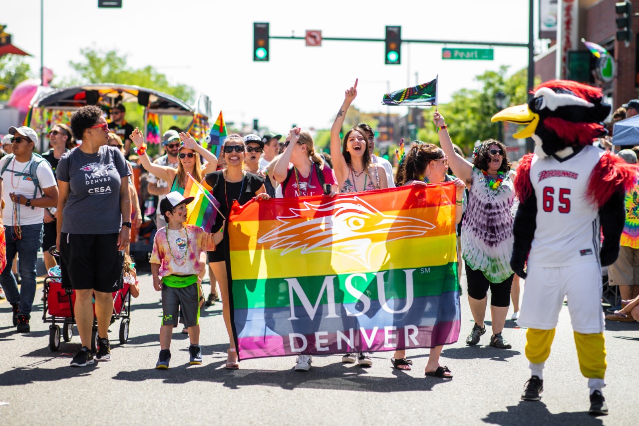 MSU Denver people in the Denver Pride Parade with a Rainbow MSU Denver flag.