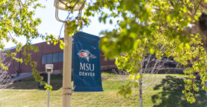 Blue MSU Denver banner in front of building surrounded by green trees.