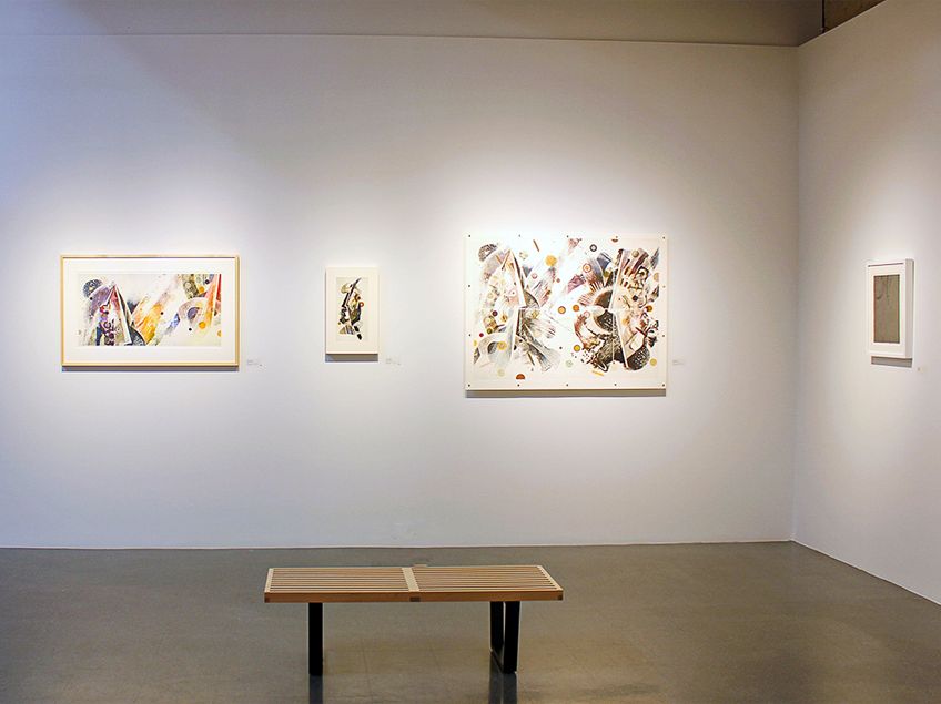 An art gallery wall displaying four abstract artworks with a wooden bench in front.