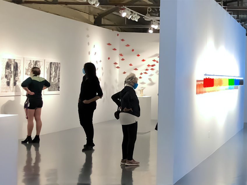Art gallery with people viewing monochrome sketches and a colorful gradient installation.