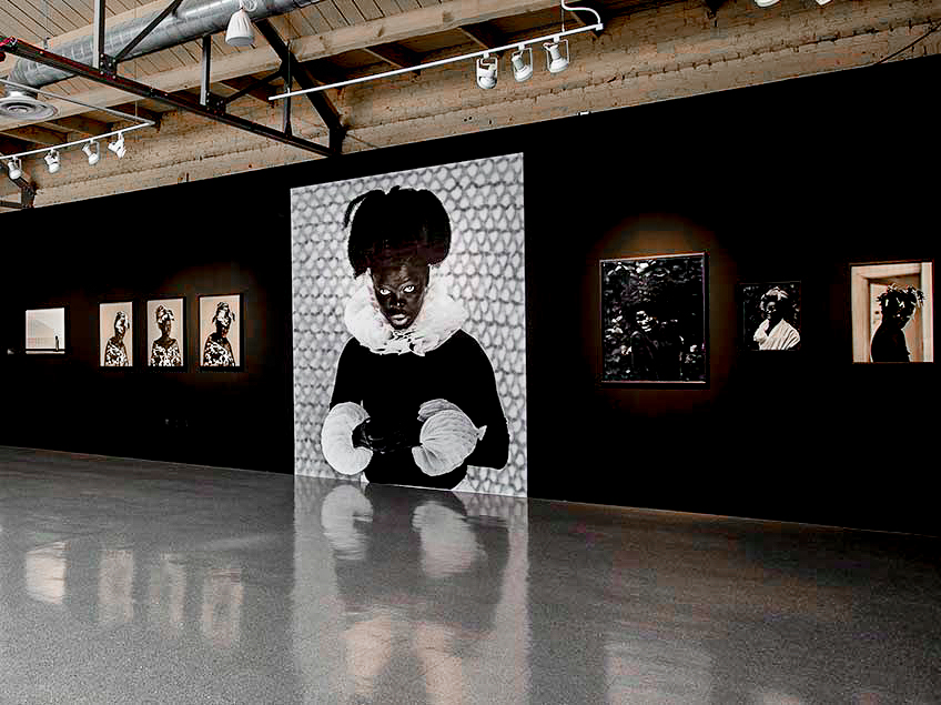 An art gallery with dark walls featuring a large black and white portrait and several smaller framed photographs.