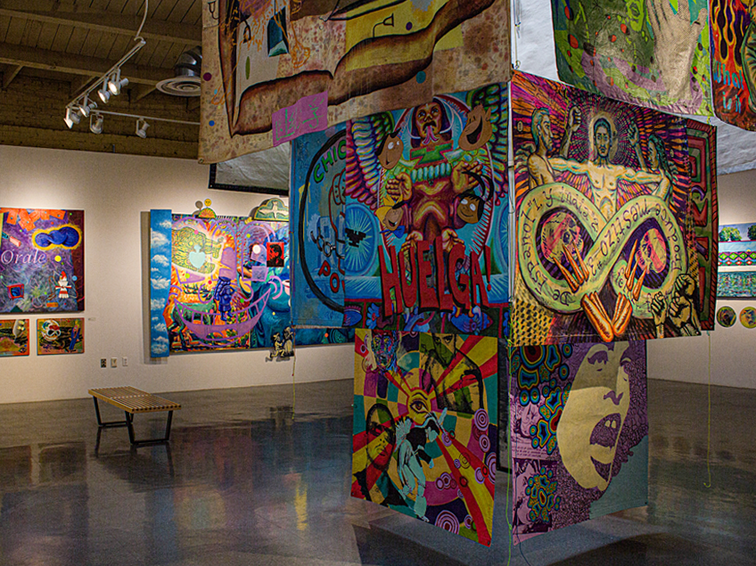 An art gallery with vibrant, colorful paintings displayed on walls and hanging from the ceiling.