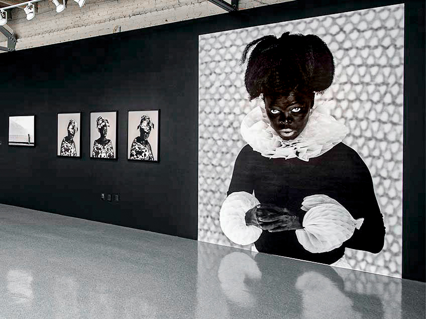 Art gallery with framed photographs on a black wall, including a large black-and-white portrait.