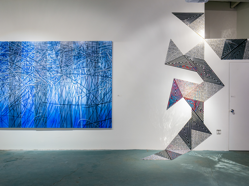 Gallery wall displaying two abstract artworks: one featuring a series of textured blue shades, and the other a geometric design in black, grey, and white tones.