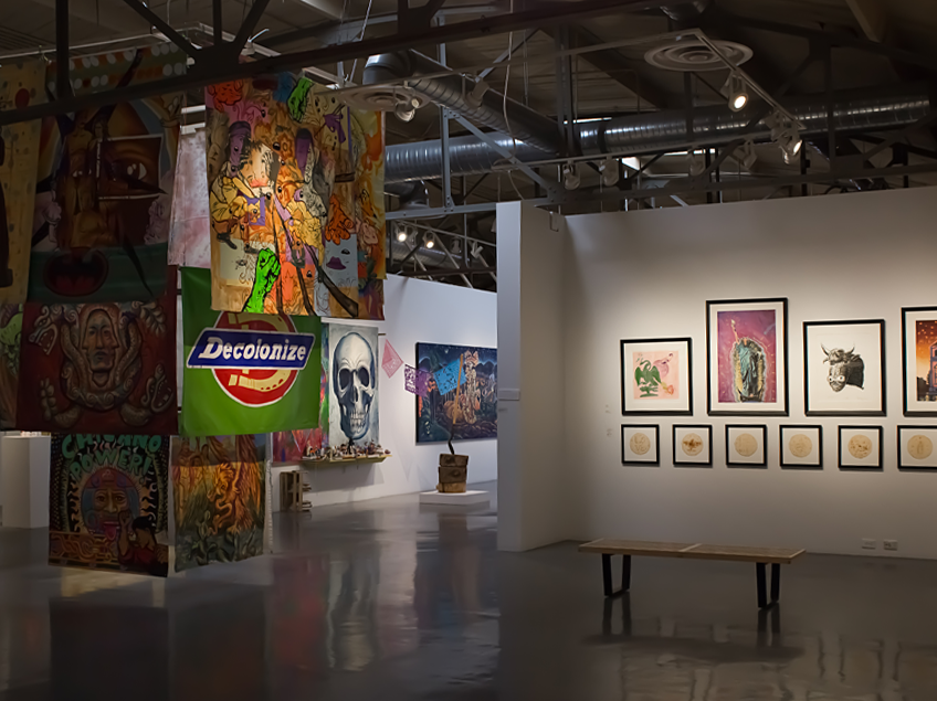 Art gallery interior with colorful banners, a skull graphic, and framed artworks displayed on walls.