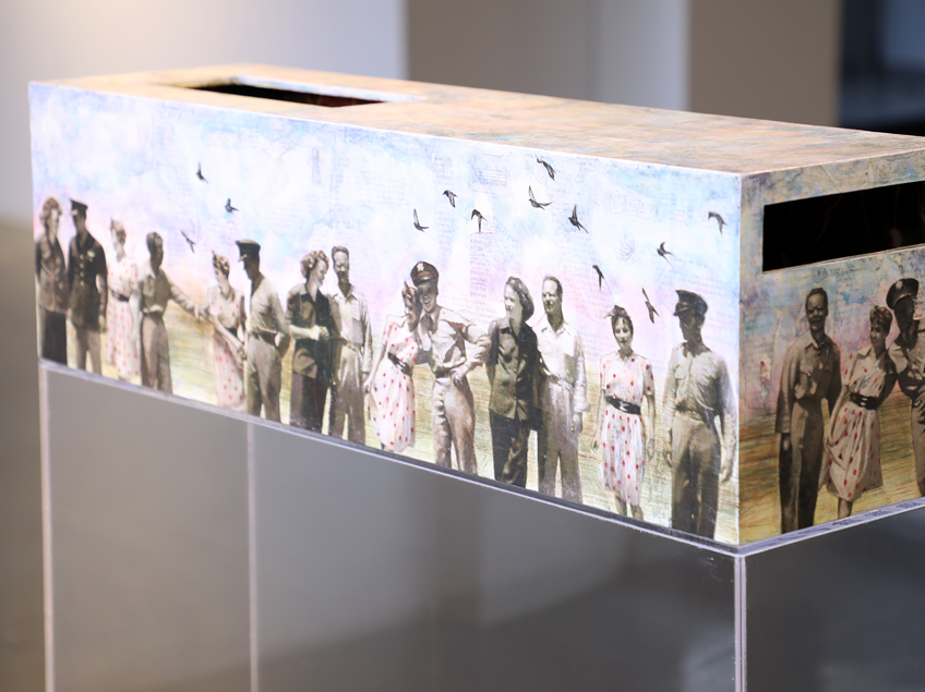 Rectangular sculpture wrapped in a vintage photograph, depicting people and birds, with a slot on top and on the side.