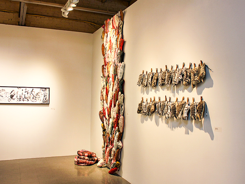 An art exhibit with colorful textile forms resembling animals displayed vertically and horizontally on walls.
