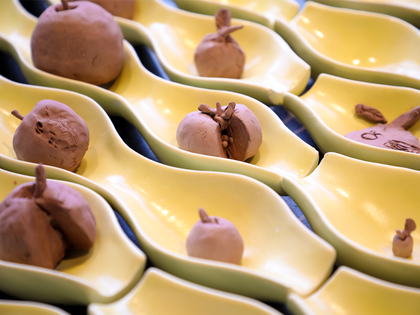 Yellow ceramic dishes with small brown clay fruit type objects arranged in a pattern.
