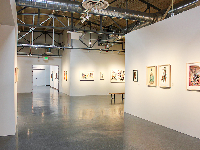 A modern art gallery interior with artworks on white walls, a polished floor, and exposed ceiling ductwork.